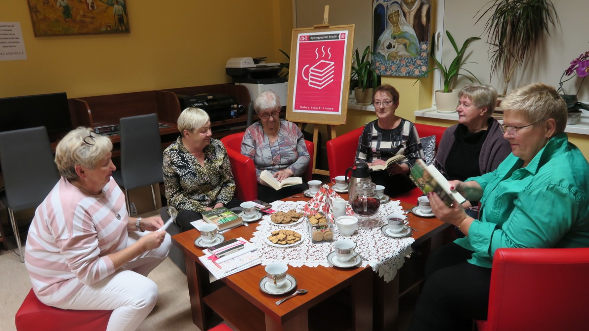 Dyskusycjny Klub Książki w Kobylnicy. Grupa osób dyskutujących o książce, siedząca przy stole